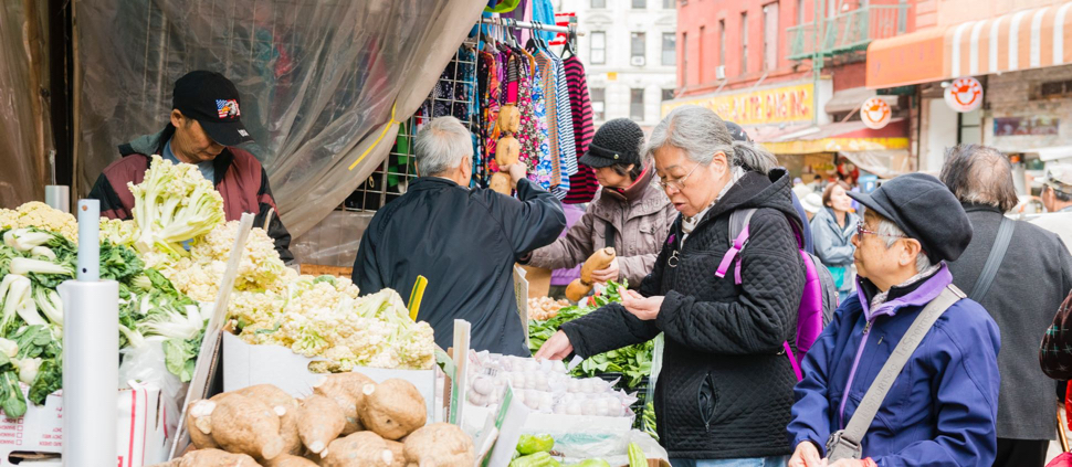 Image of older adult Asian women purchasing vegetables from storefront 