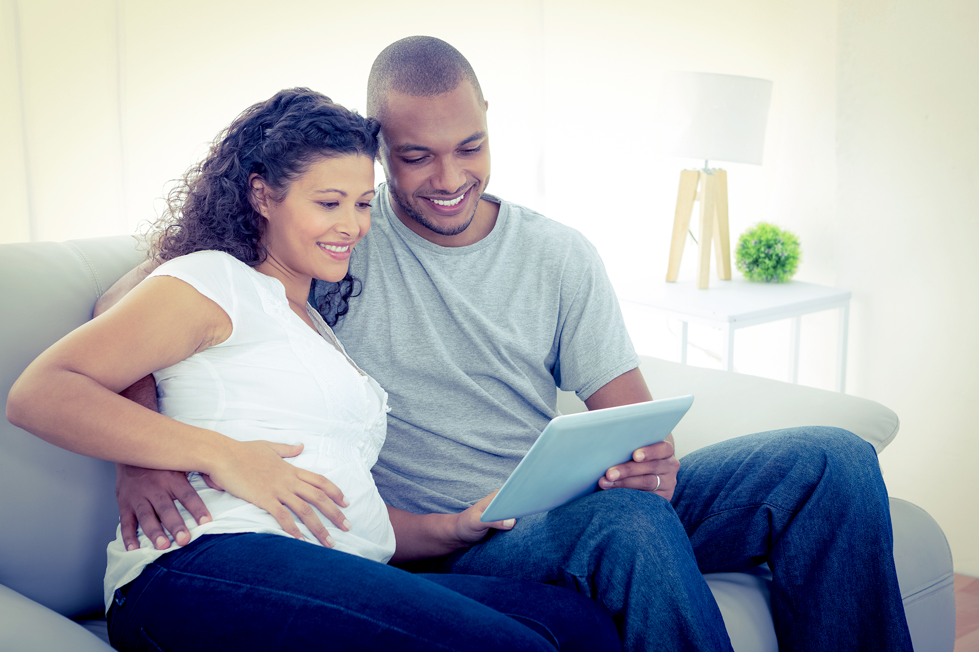 Una mujer embarazada y un hombre sentados en un sofá viendo una tableta. 