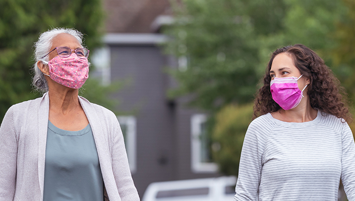 Two women walking outside wearing masks.