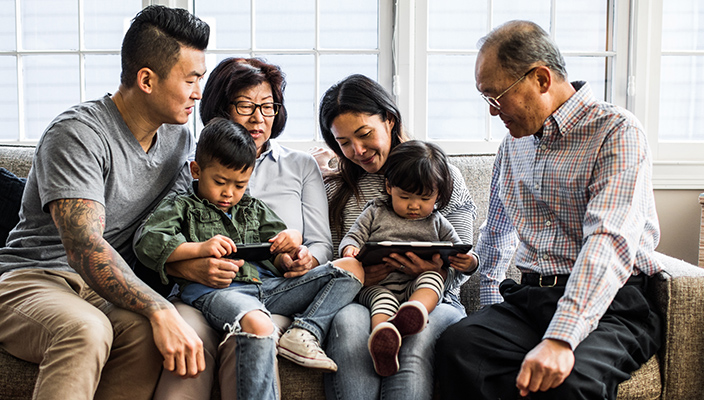 Una familia sentada en un sofá, sosteniendo a dos niños pequeños que miran dispositivos electrónicos portátiles.