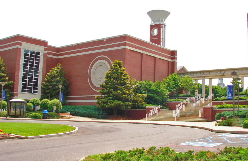 Large brick university building with a grand staircase and circular driveway.