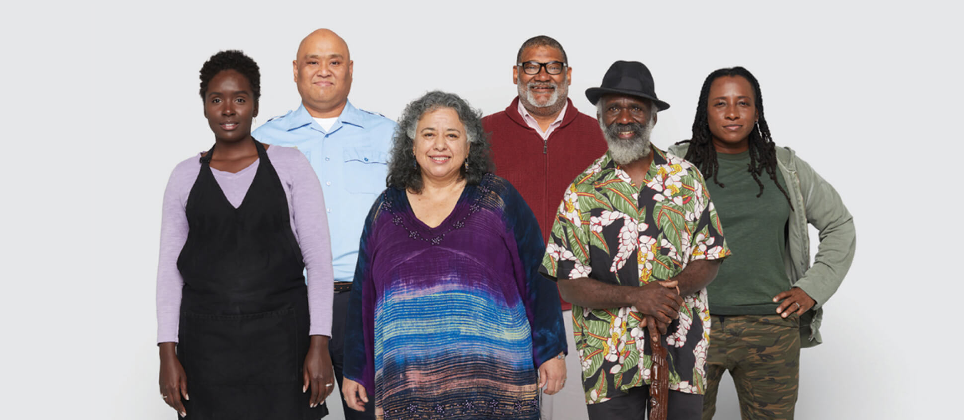 Six adults of different ages and ethnicities stand together, smiling at the camera.