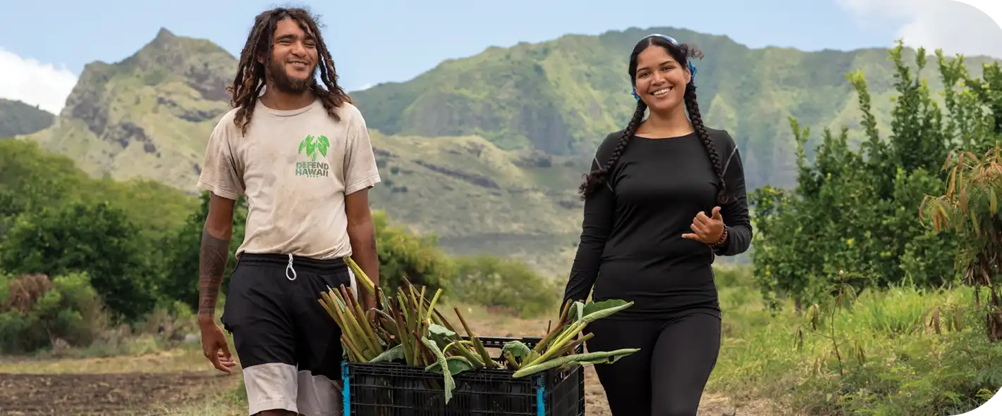 A male and female farmer in Hawaii carrying a basket of plants